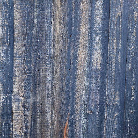 Black finish reclaimed redwood S3S wall planks laid flat, grain and saw marks visible through the pigment